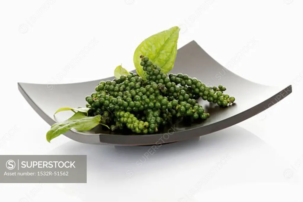 Clusters of green peppercorns with leaves in dish