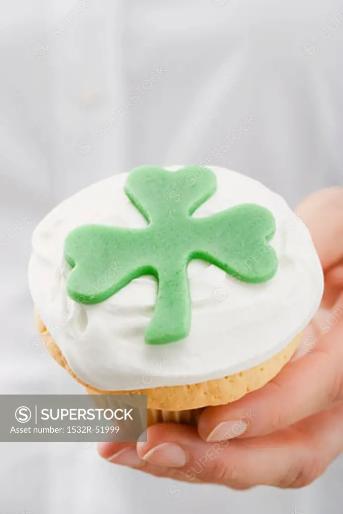 Hand holding cupcake with marzipan clover leaf