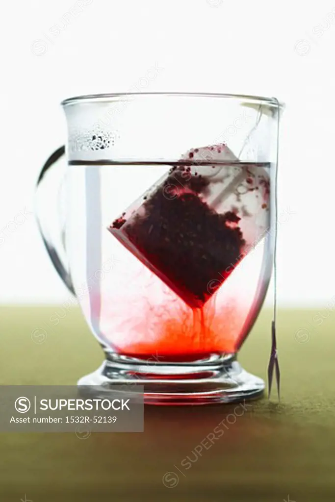 Red Tea Bag Steeping in Glass Mug