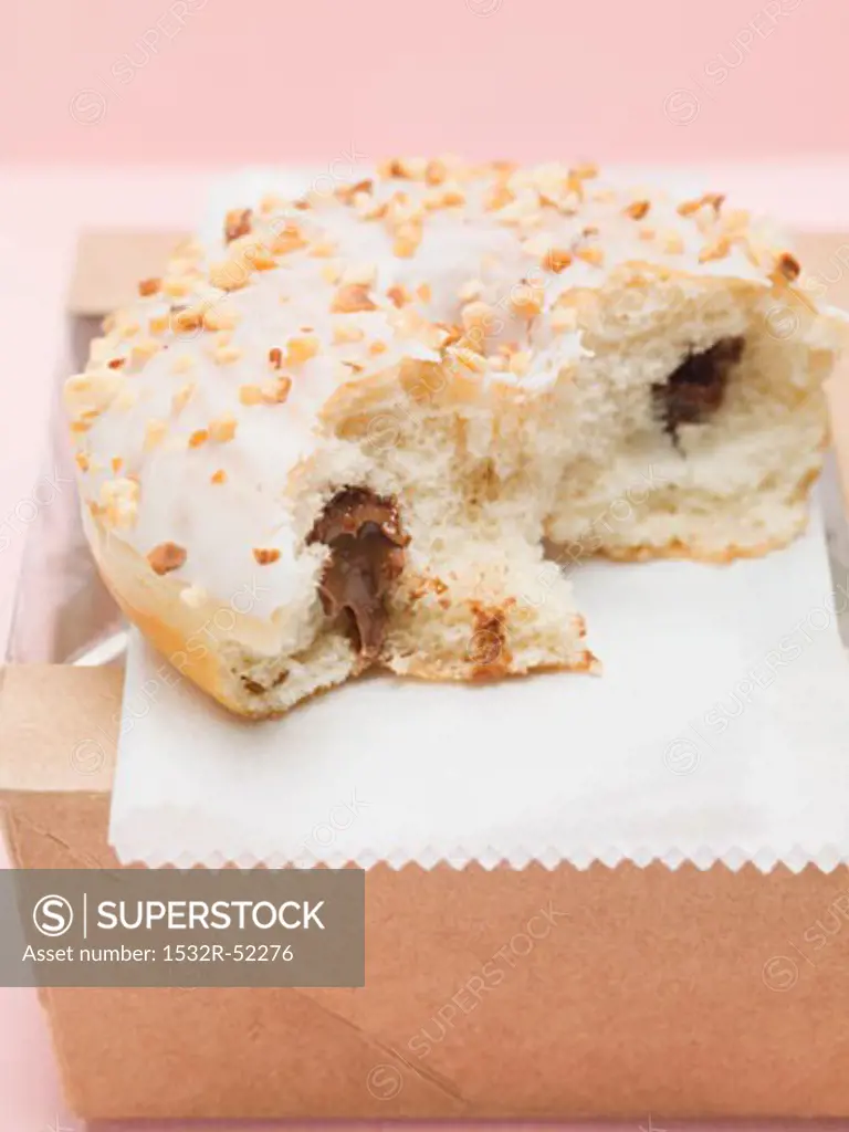 Iced doughnut with chocolate filling & chopped nuts, a bite taken