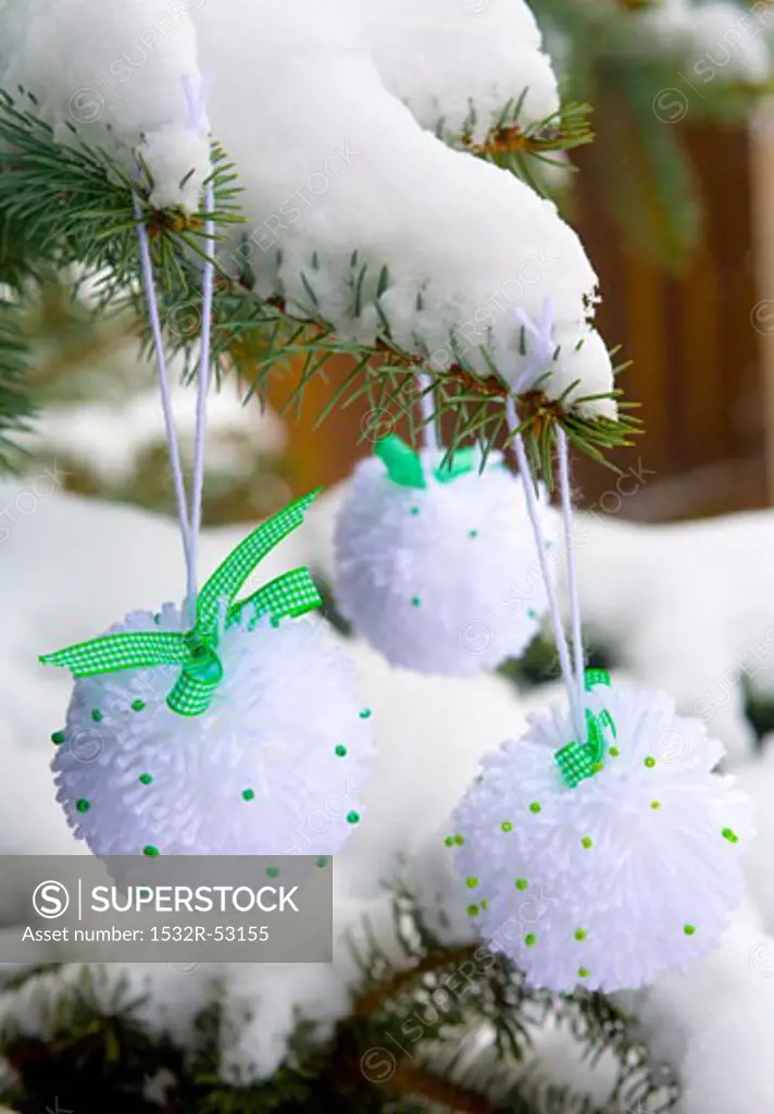 Snowball pompoms hanging on a snow-covered fir branch