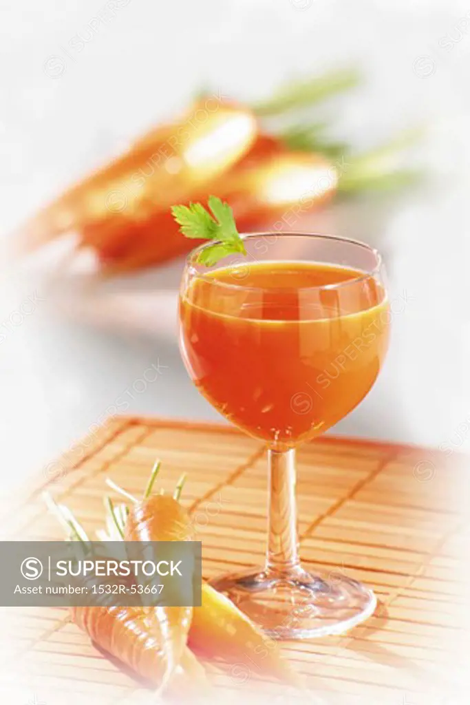 Carrot juice in glass, fresh carrots beside it