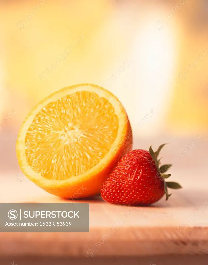Half an orange and a strawberry on wooden board