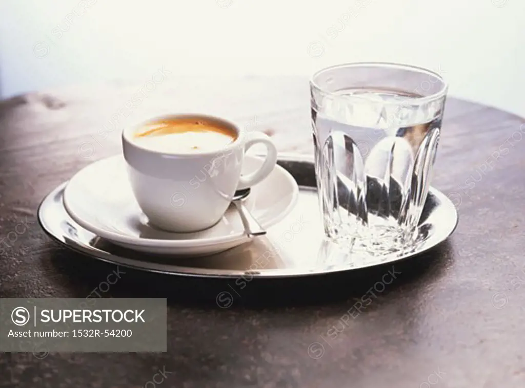 A cup of coffee and a glass of water on a silver tray