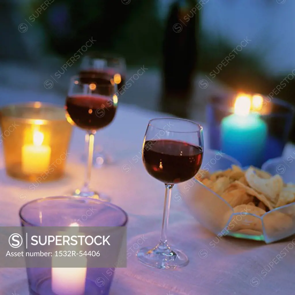 Glasses of red wine and crisps on candlelit table