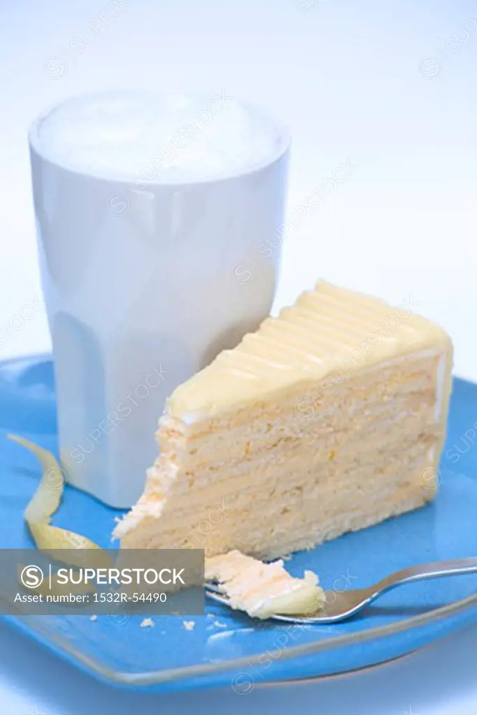 A large beaker of milky coffee & a piece of lemon cream cake