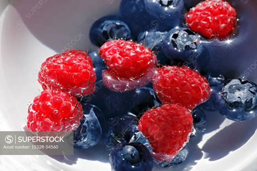 Raspberries and blueberries in a bowl of water