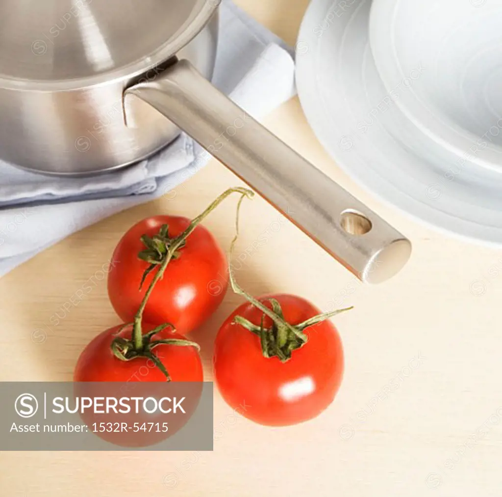 Three tomatoes beside pan and plates
