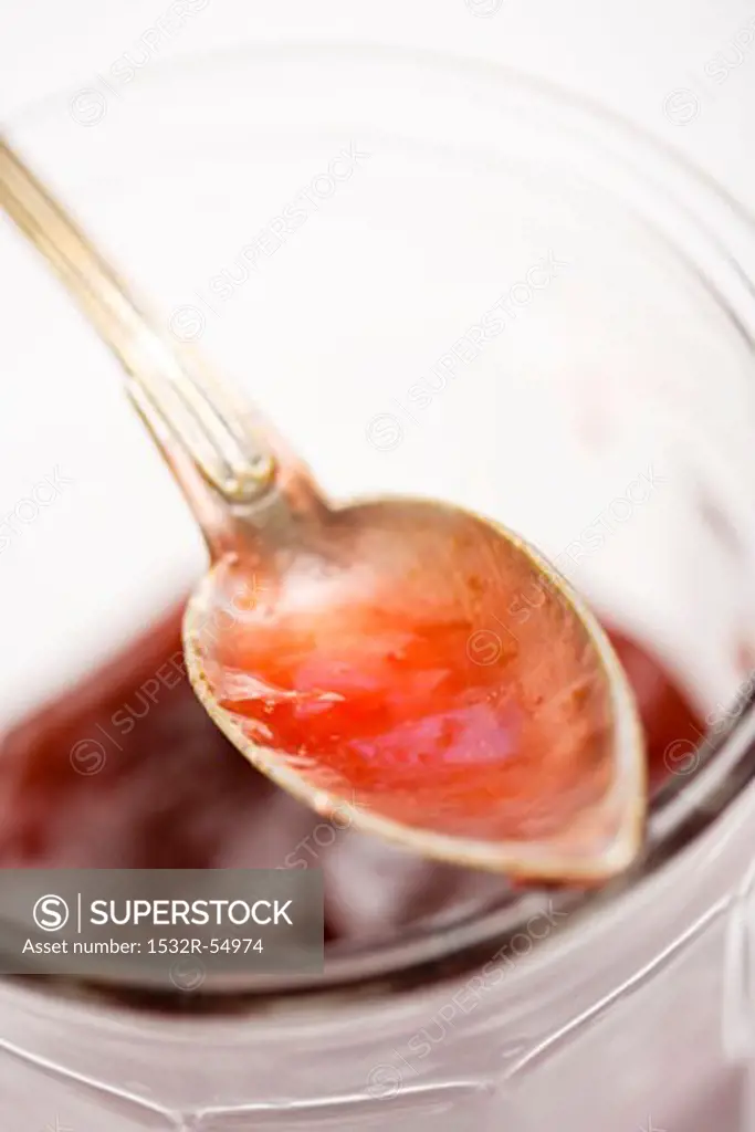 Silver spoon with remains of plum jam on screw-top jar