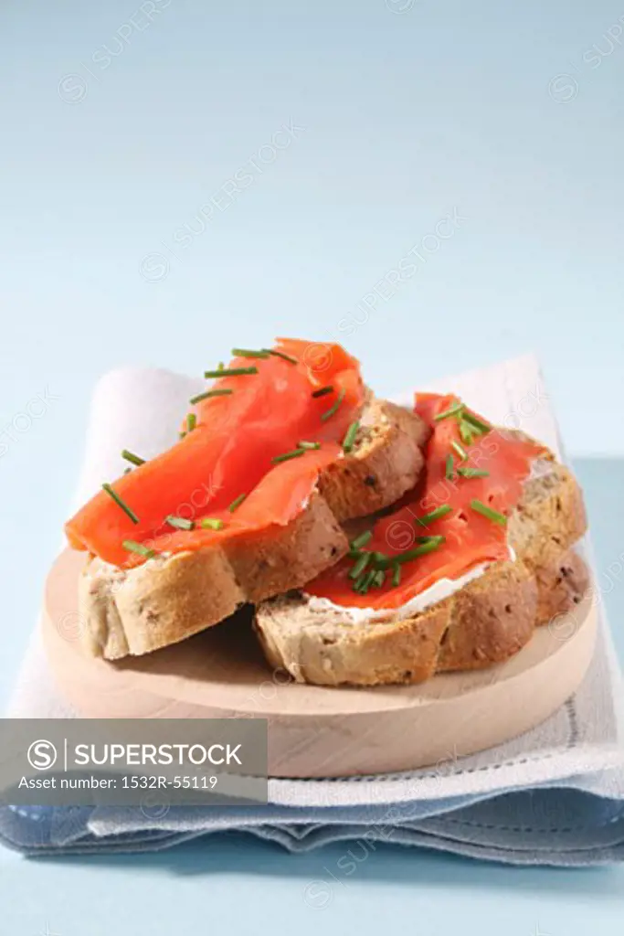 Two slices of bread with smoked salmon and chives on a wooden plate