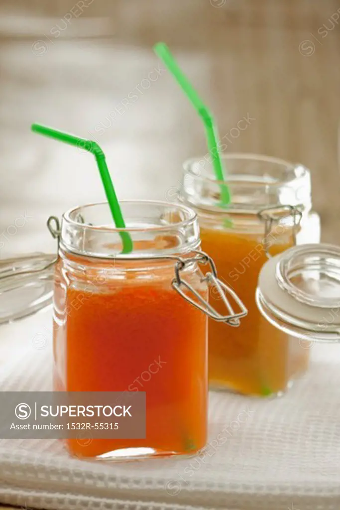Carrot and orange juice and peach juice in preserving jars with straws