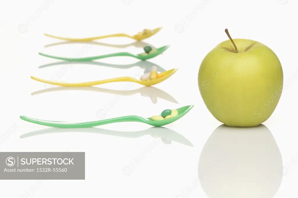 Spoons with vitamin tablets and a green apple
