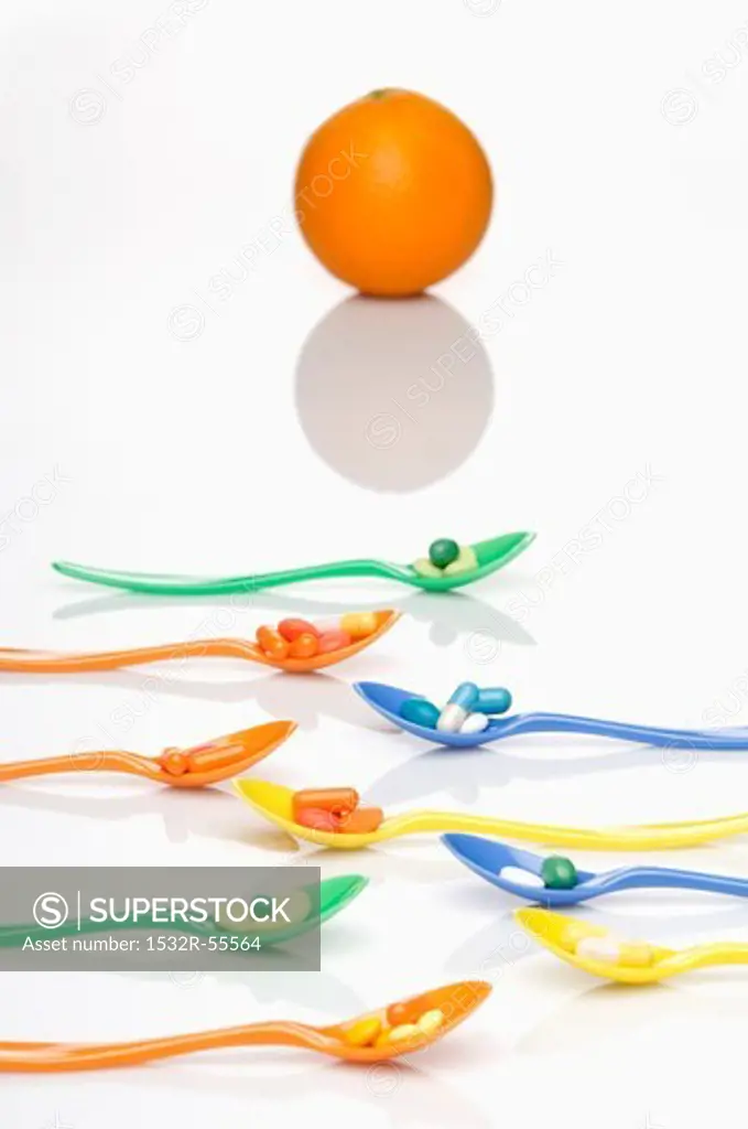 Spoons with vitamin tablets with an orange in the background