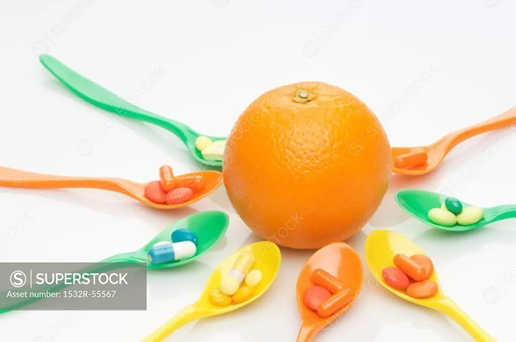 Spoons with vitamin tablets around an orange