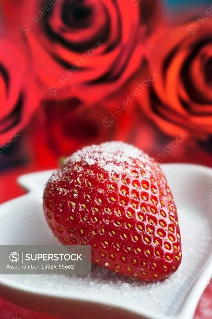 A sugared strawberry with roses in the background