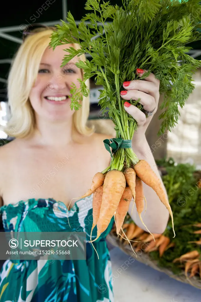 A woman holding a bunch of carrots at a market