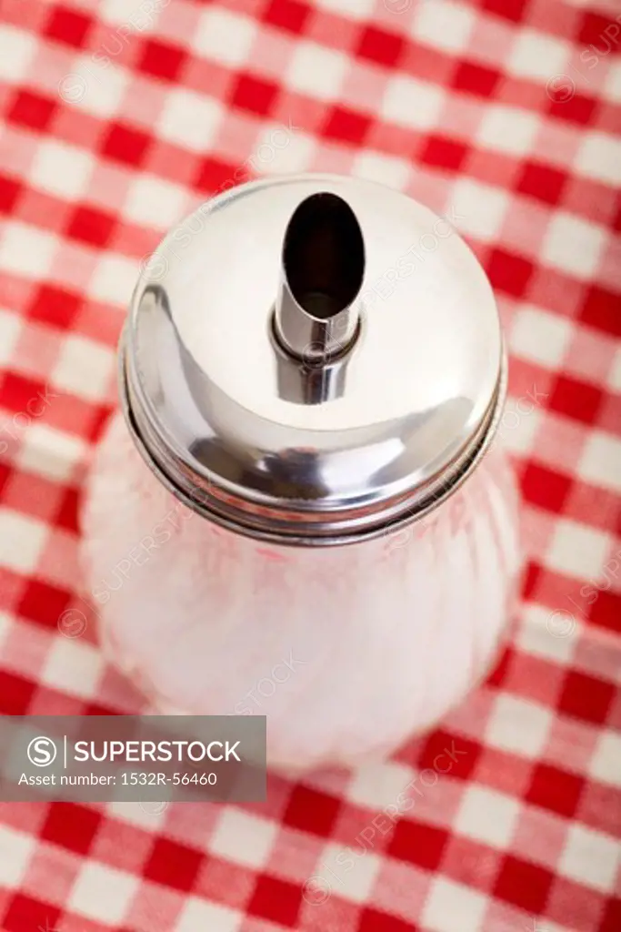 A sugar pourer on a checked table cloth