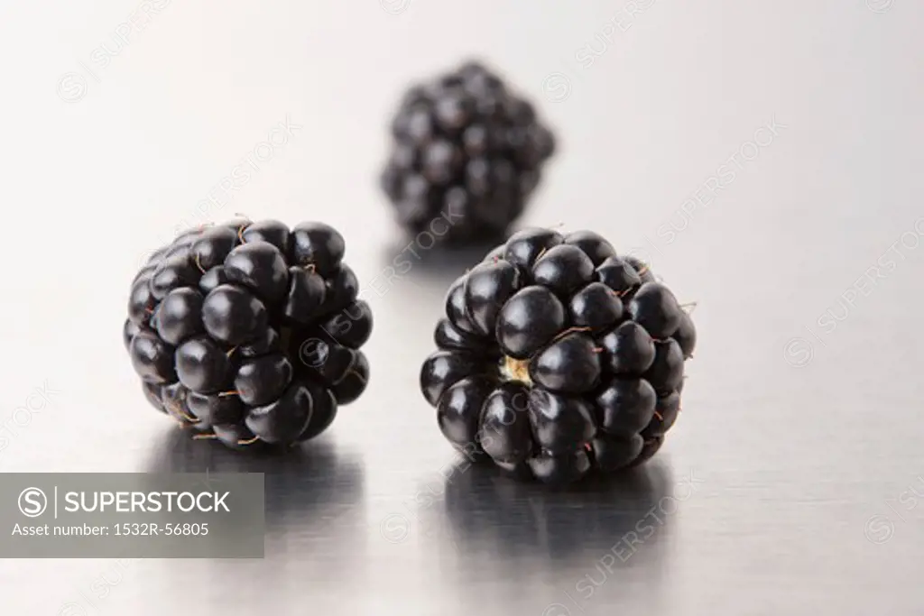 Three blackberries on a metal surface (close-up)