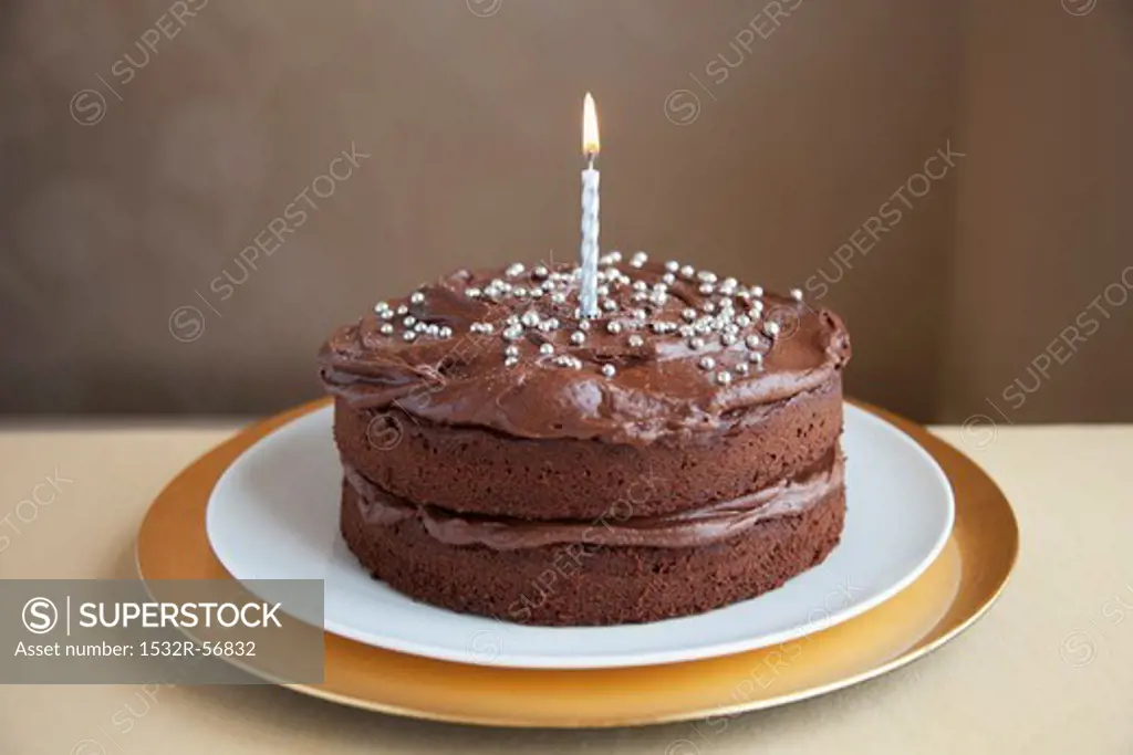 A chocolate cake decorated with silver balls and a candle