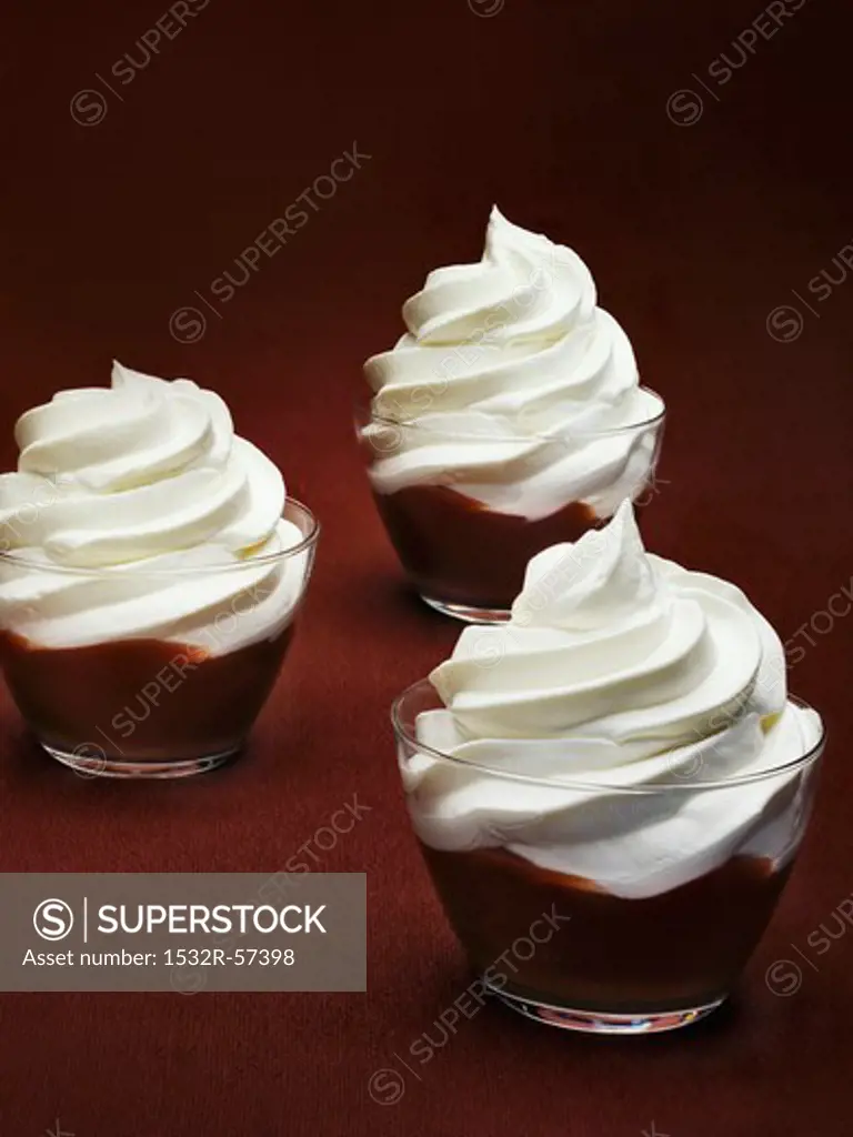 Three glasses of chocolate pudding topped with cream