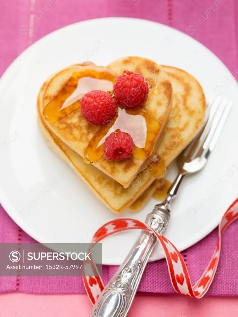 Heart-shaped pancakes with raspberries and maple syrup
