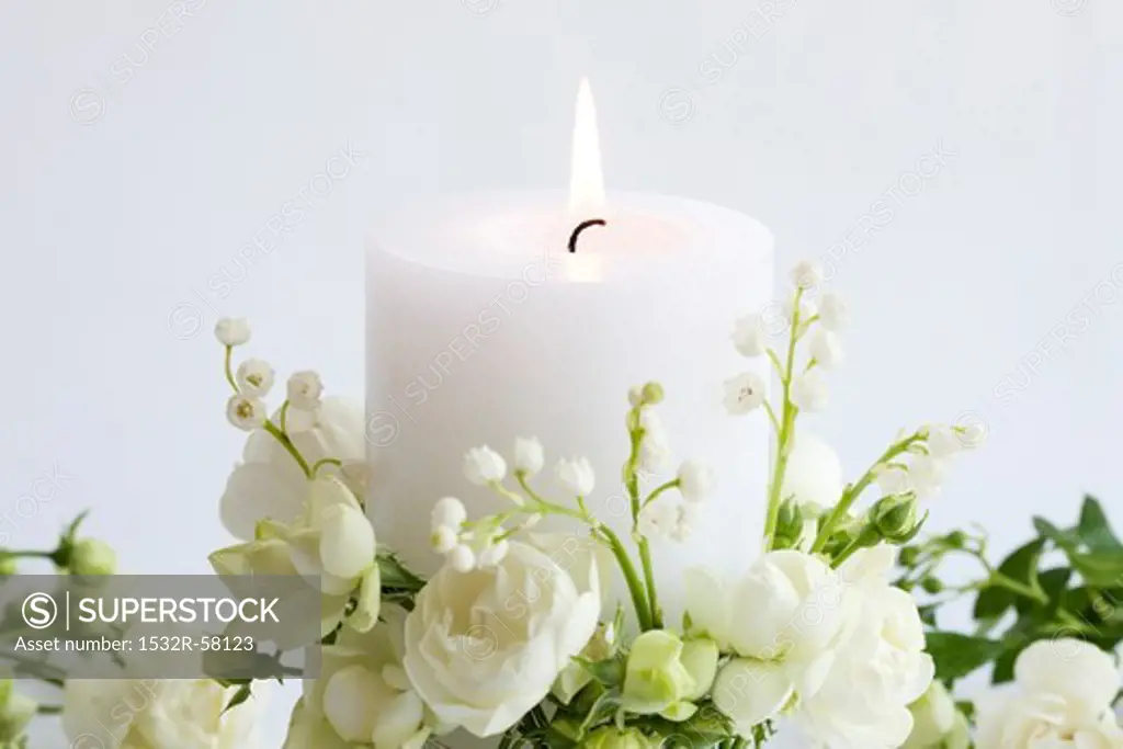 Burning white candle with white roses and lilies of the valley