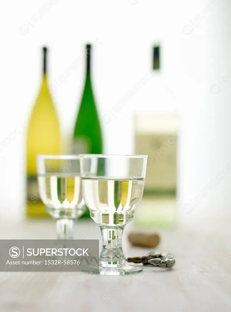 Glasses of white wine, a cork screw and bottles of wine