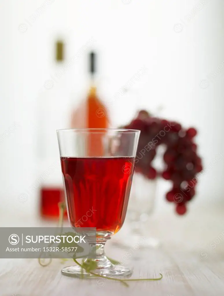 A glass of red wine, red grapes and bottles of red wine