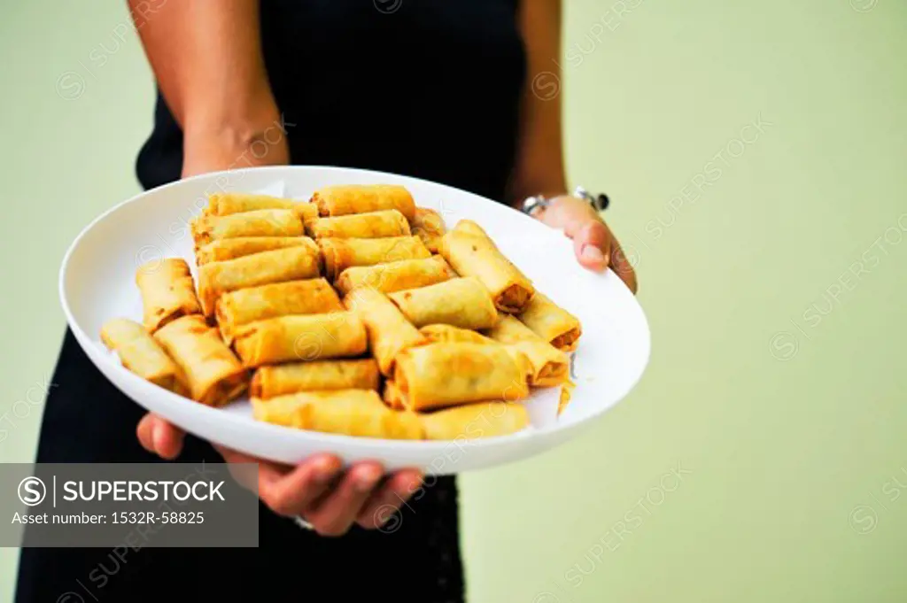 A woman holding a plate of spring rolls