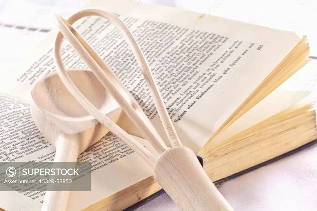 A cookbook, a whisk and a wooden spoon