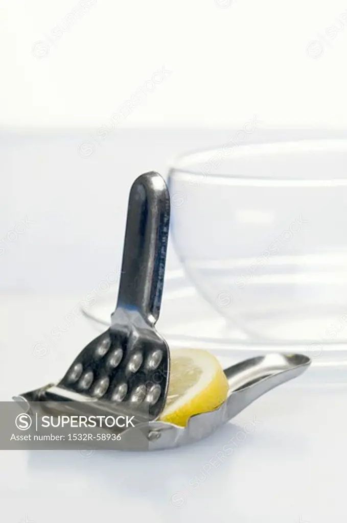 A lemon press with a slice of lemon and a tea glass in the background
