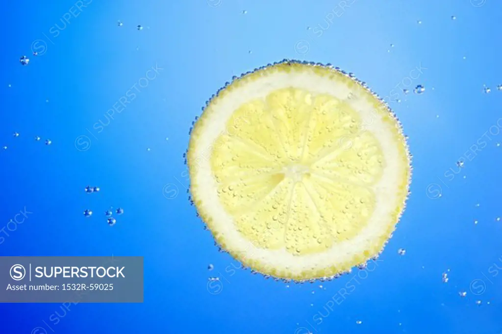 A slice of lemon in blue water with air bubbles