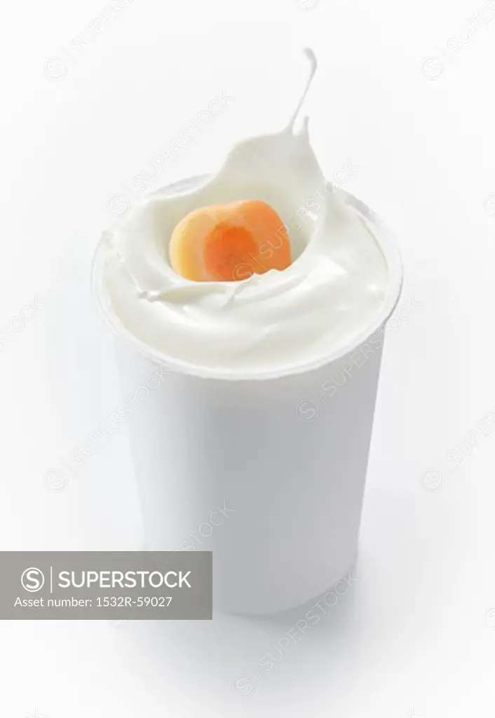 An apricot falling into a cup of yogurt