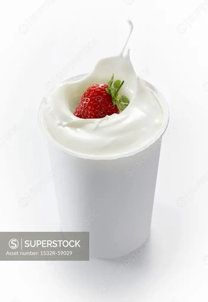 A strawberry falling into a cup of yogurt