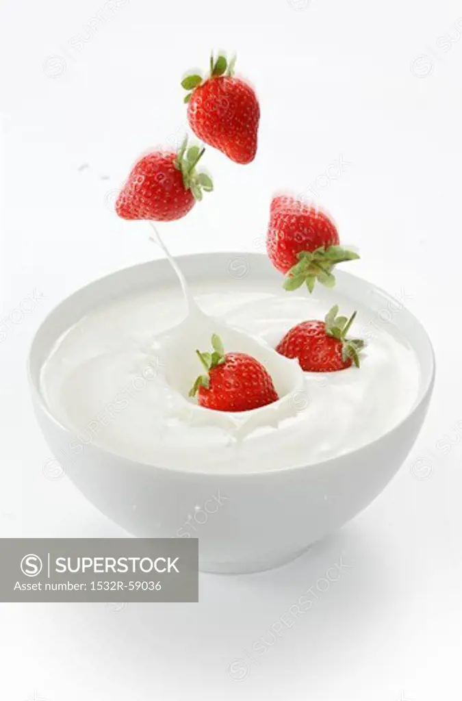 Strawberries falling into a bowl of yogurt