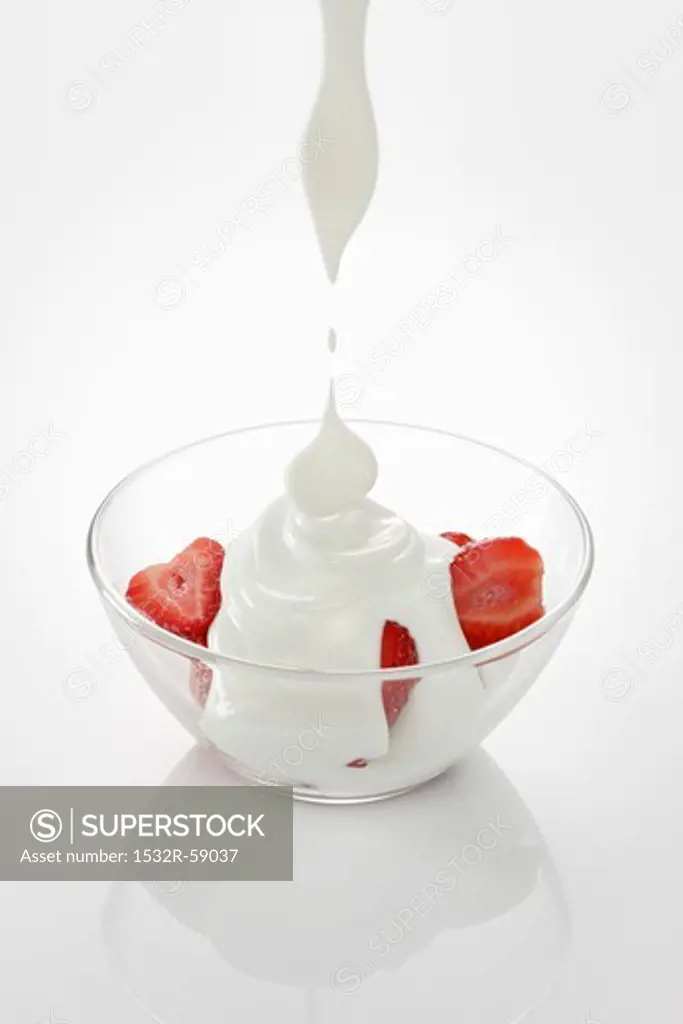 Yogurt dripping onto strawberries in a glass bowl