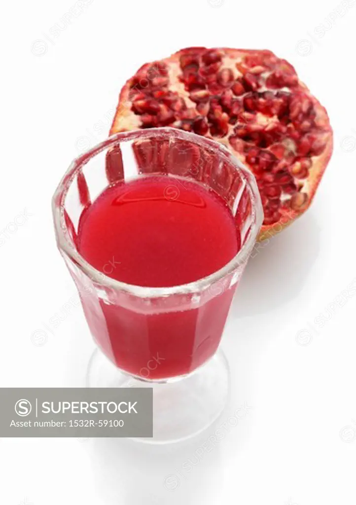 A glass of pomegranate juice with half a pomegranate in the background