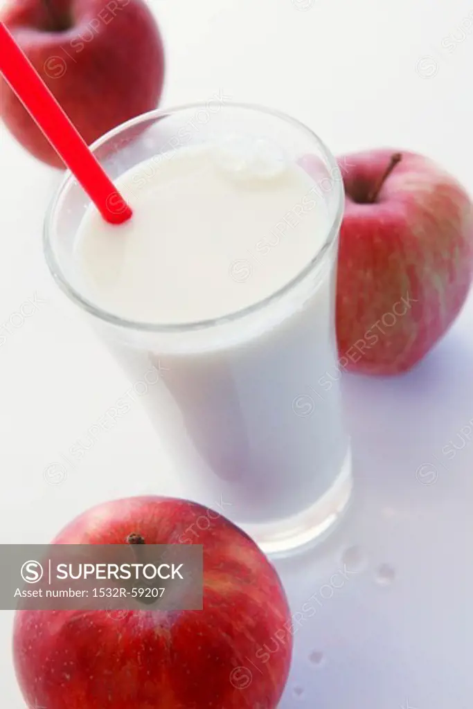 A glass of milk with a straw and three red apples