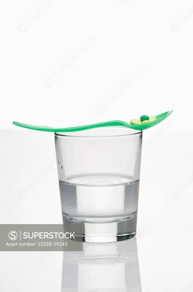 A vitamin pill on a spoon on a glass of water