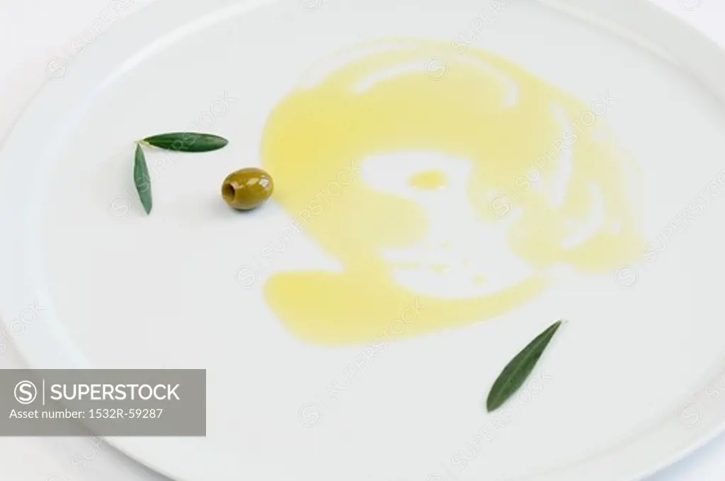 Olive oil, green olives and olive leaves on a plate