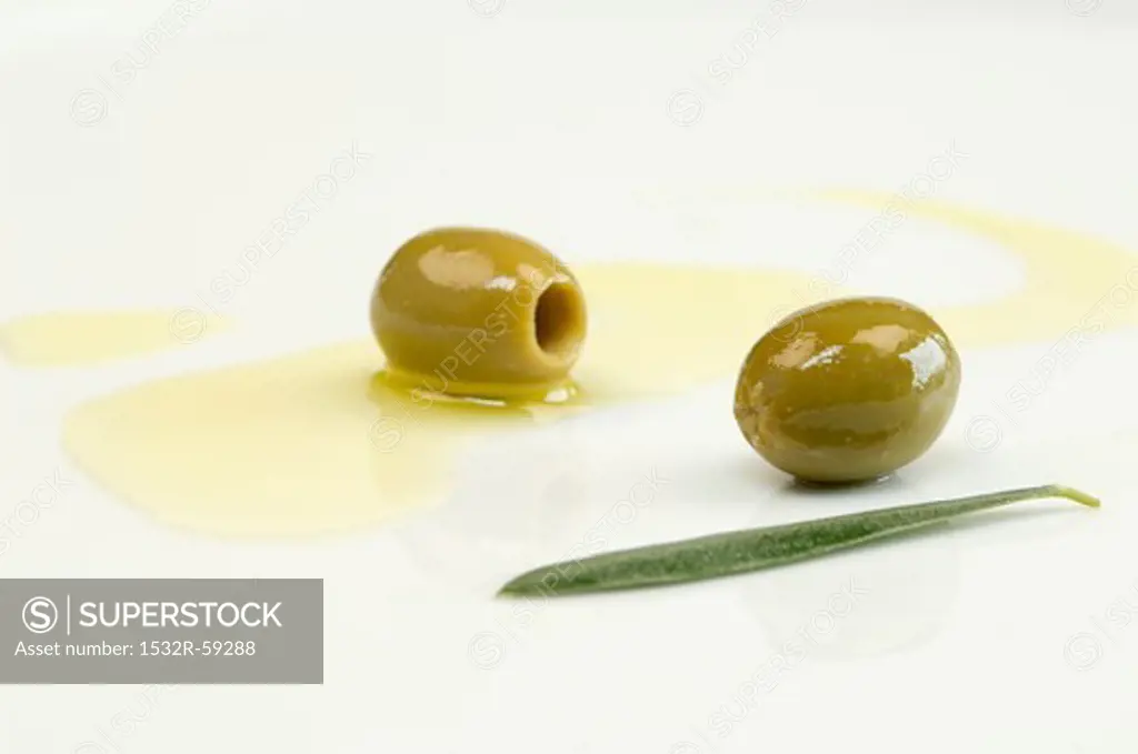 Olive oil, green olives and an olive leaf on a plate