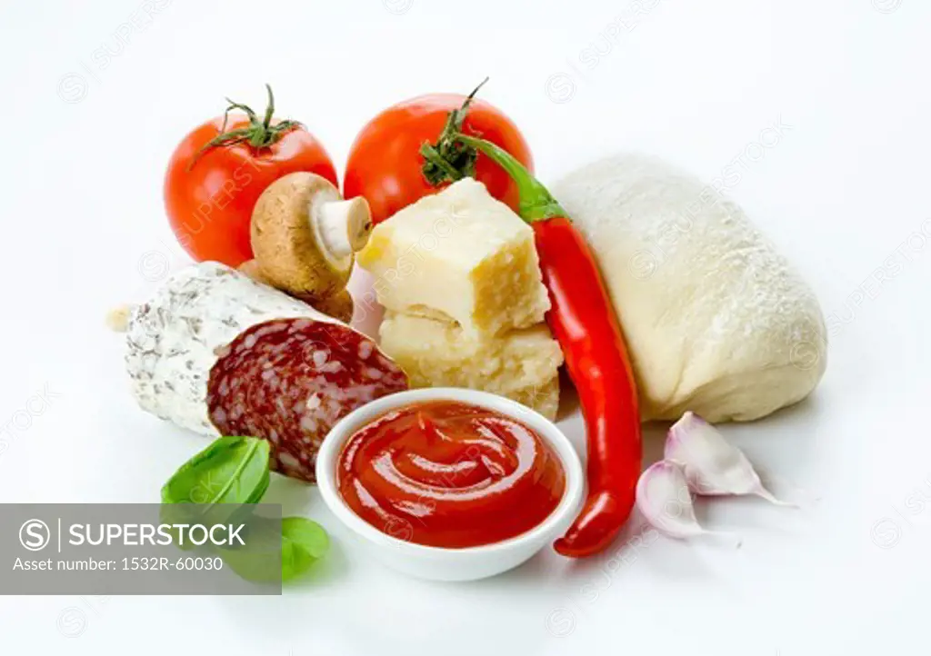 Pizza ingredients: tomatoes, a ball of dough, parmesan, Italian salami, garlic, ketchup, mushrooms