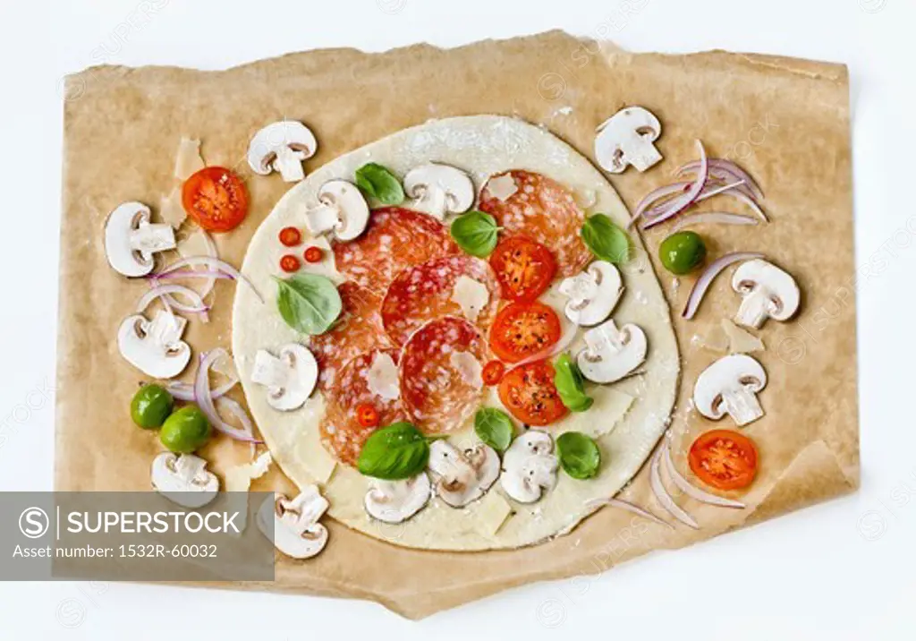 A raw pizza with salami and mushrooms on baking paper