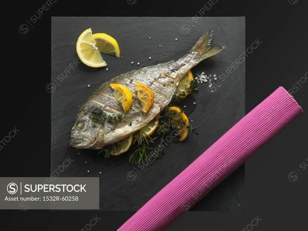 Fried bream with lemons and herbs on a slate plate