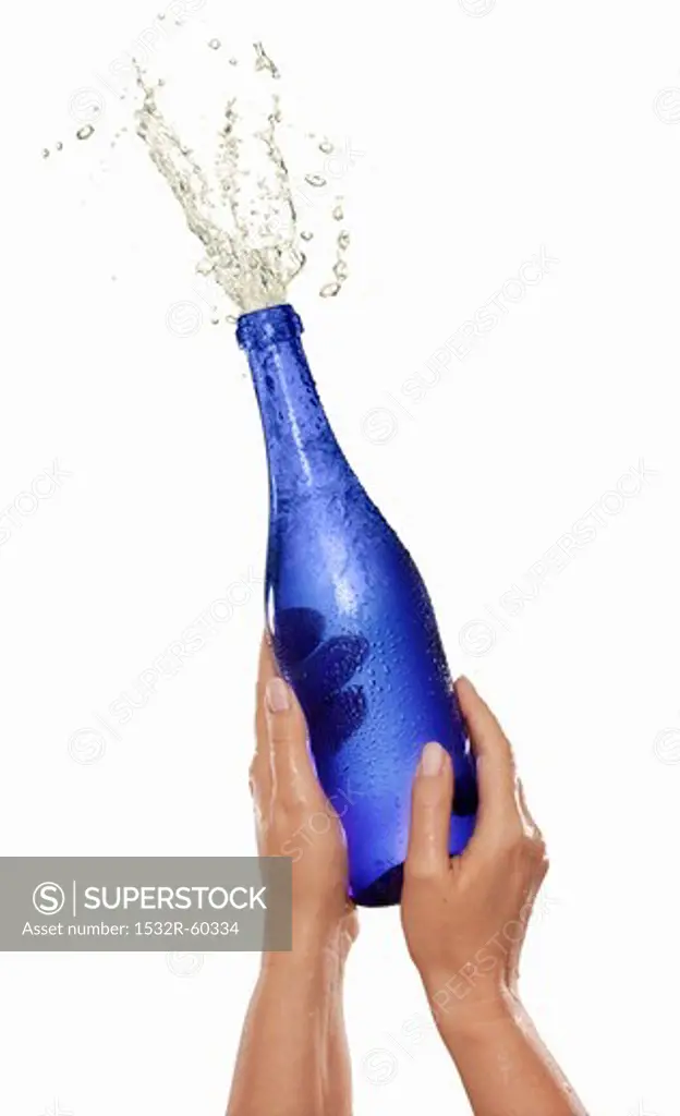 Hands holding a spraying champagne bottle