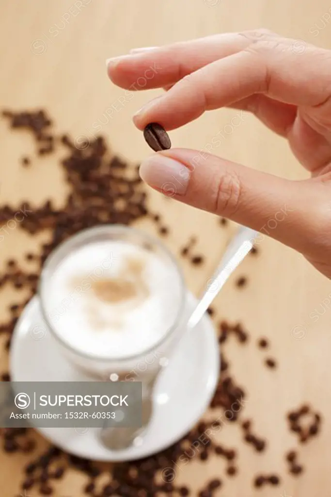 Fingers holding a coffee bean over a glass of Latte Machhiato