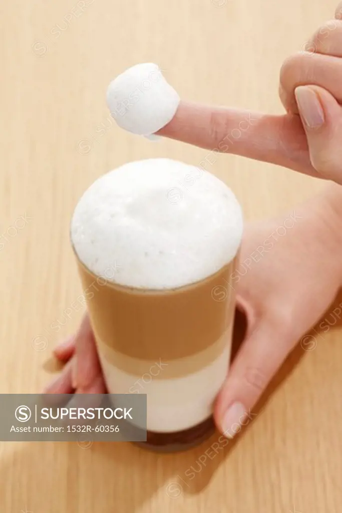 Milk foam covered finger from a glass of Latte Macchiato