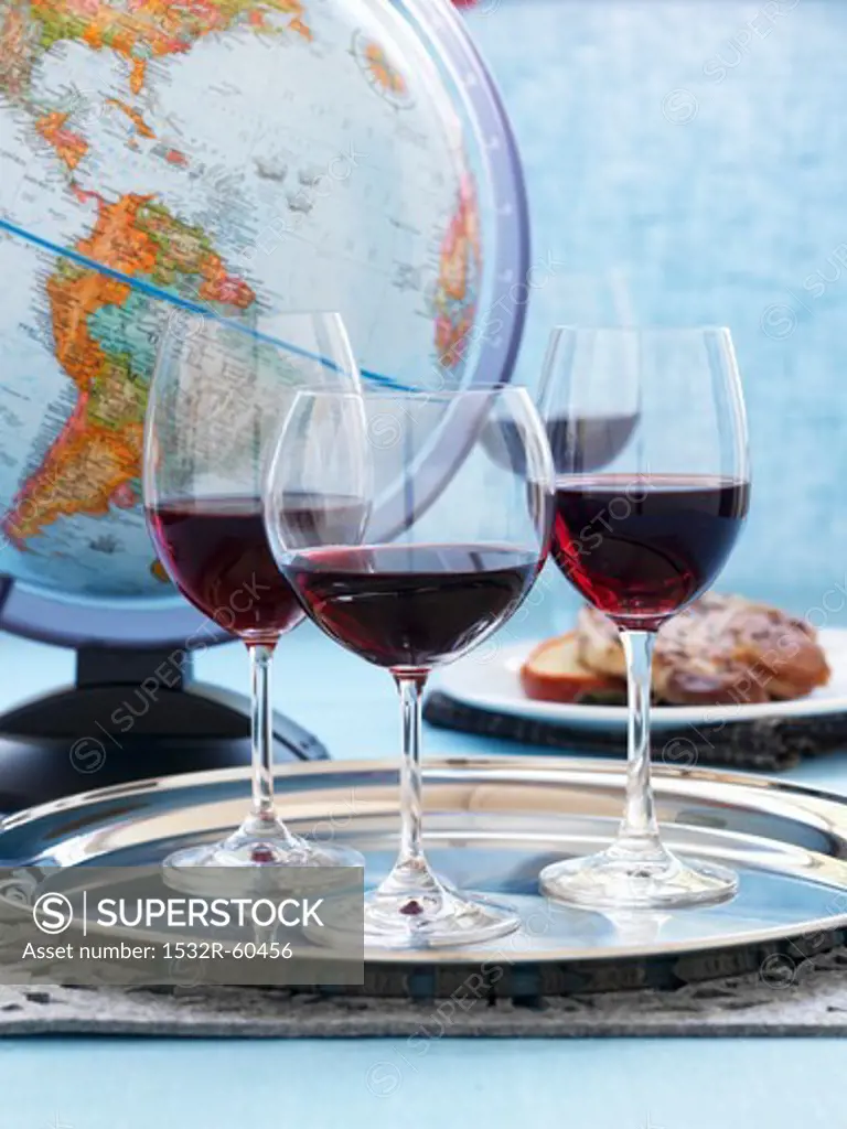 Three glasses red wine on a silver platter in front of a globe