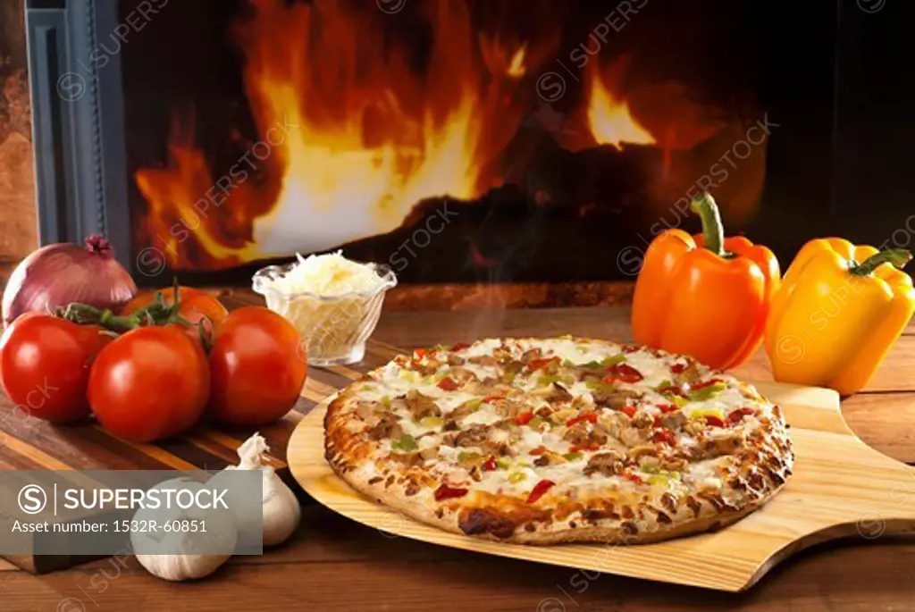 A chicken and vegetable pizza on a pizza paddle in front of a wood-fired oven