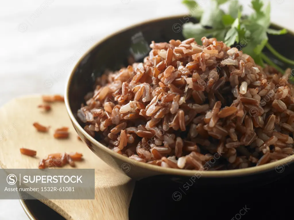 Bowl of Cooked Red Rice; Wooden Spoon